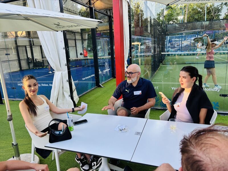 Guests chatting at a table beside the padel courts